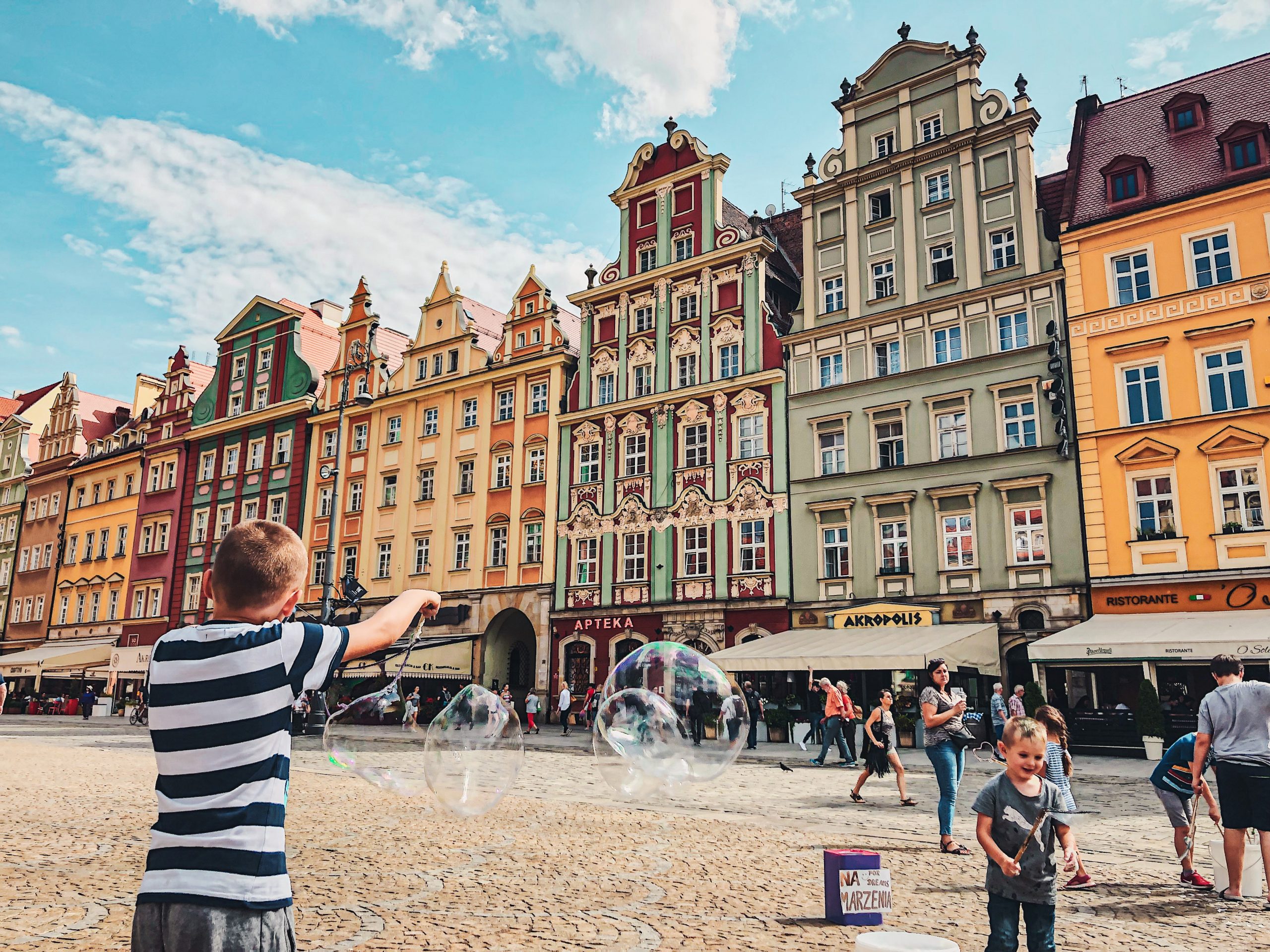 A boy is playing with soap bubbles in front of buildings in Wroclaw Poland